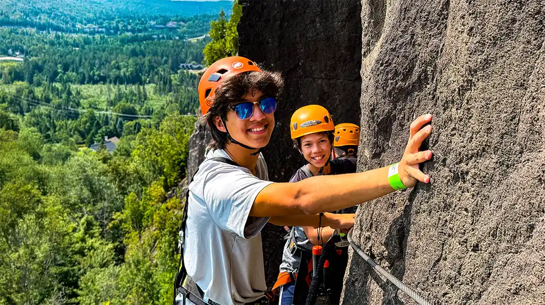 Two boys cling to the side of a cliff on a Via Ferrata in Quebec